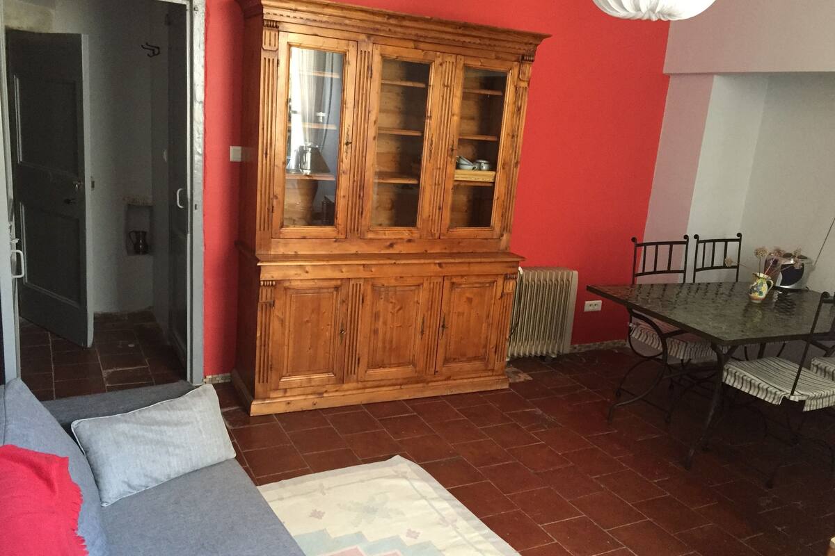 Una habitación con un armario de madera, una mesa de comedor con sillas, un radiador y un sofá con cojines.