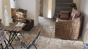 A rustic interior with a wicker sofa, wooden benches, and a table with a vase. - Maison Anila (Barjac)