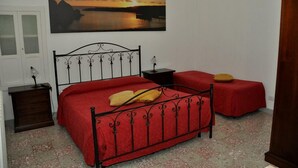 A bedroom with a bed, two bedside tables, a nightstand, a wall-mounted lamp, and a painting of a sunset over water. - Arco Michele (Putignano)