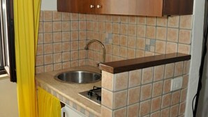 A compact kitchen with a sink, a small refrigerator, and a wooden cabinet above the countertop. - Arco Michele (Putignano)