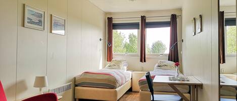 A small, well-lit room with two beds, a desk, a chair, and a red armchair.