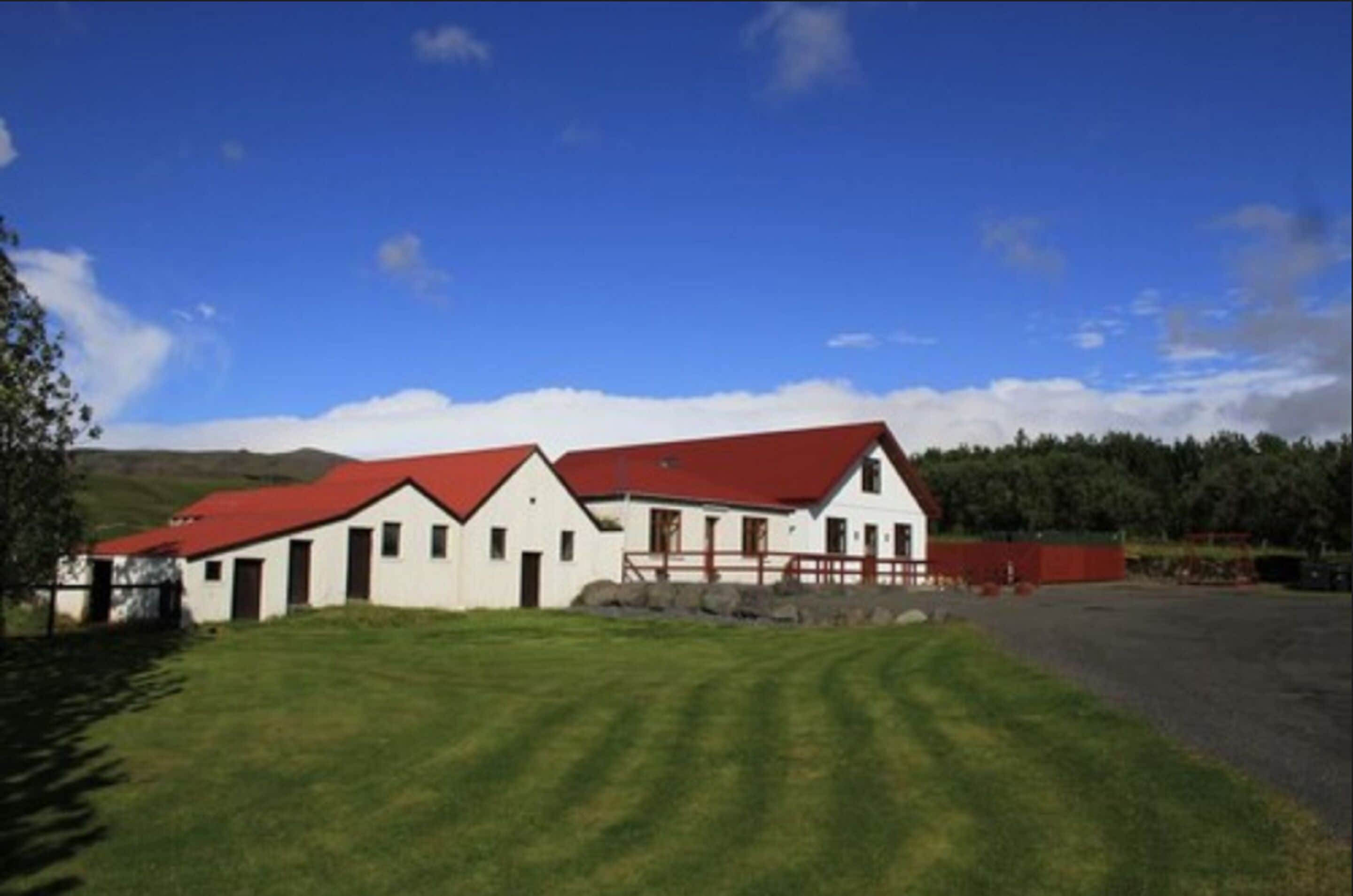 A white building with a red roof, surrounded by a well-maintained lawn and a parking area.