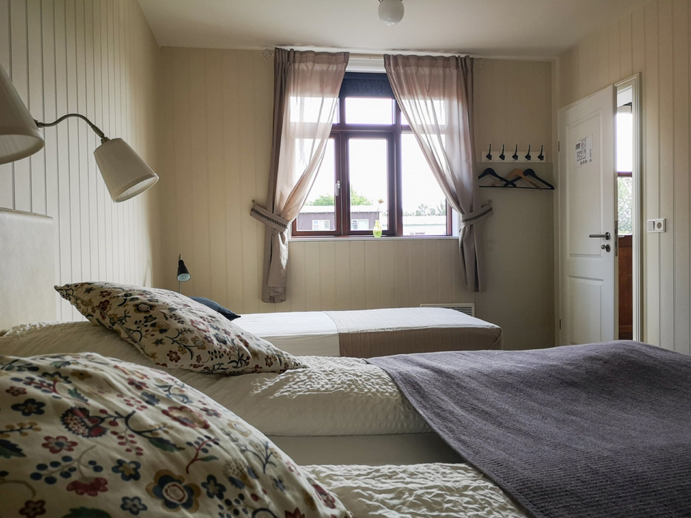 A bedroom with a bed, a bedside lamp, a window with curtains, and a coat rack.