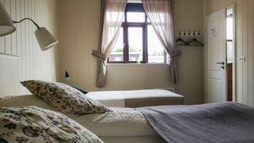 A bedroom with a bed, a bedside lamp, a window with curtains, and a coat rack.