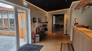 A reception area with a wooden reception desk, a fire extinguisher, a trash bin, and a door leading outside. - Sólheimahjáleiga Guesthouse (Ytri Sólheimar)