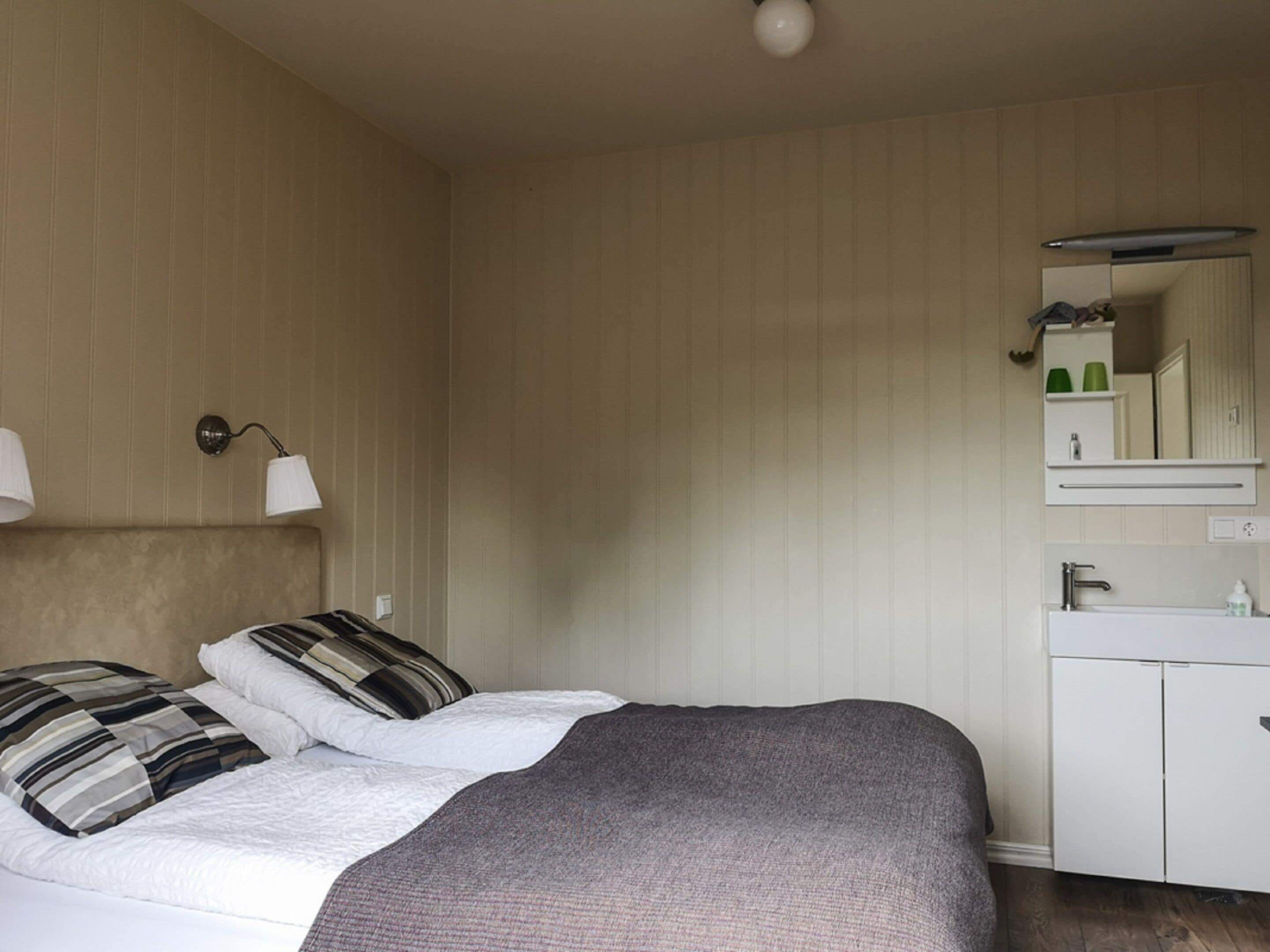 A bedroom with a bed, pillows, a bedside lamp, a dresser, a mirror, and a ceiling light.