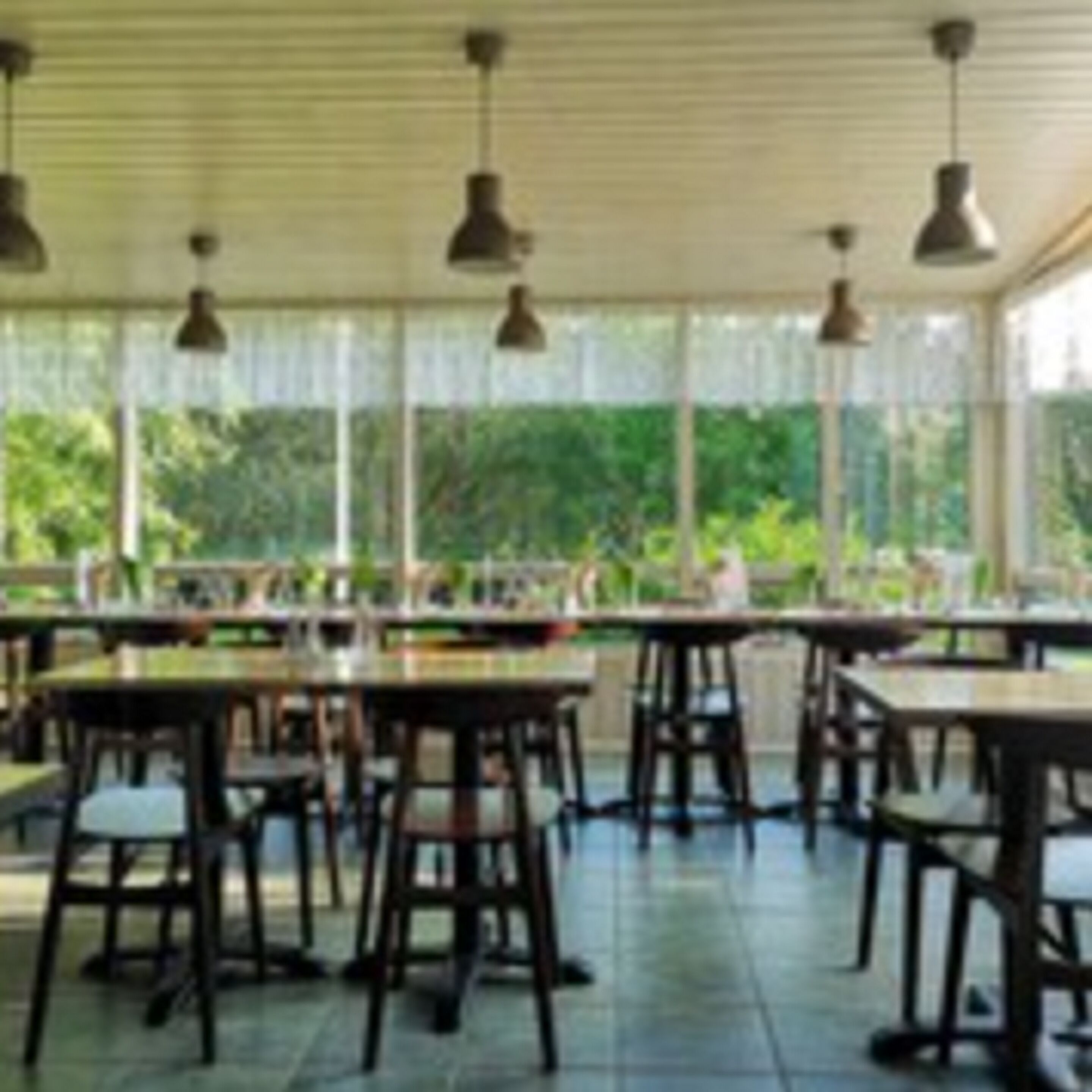 A covered outdoor dining area with tables and chairs, large windows, and hanging pendant lights.
