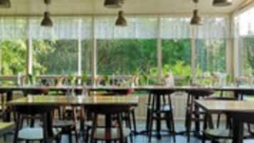 A covered outdoor dining area with tables and chairs, large windows, and hanging pendant lights.