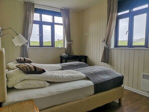 A bedroom with two beds, a bedside table, a lamp, and a view of the outdoors.