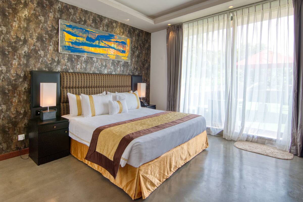 A large bed with a headboard, bedside tables, a lamp, and a window with curtains.