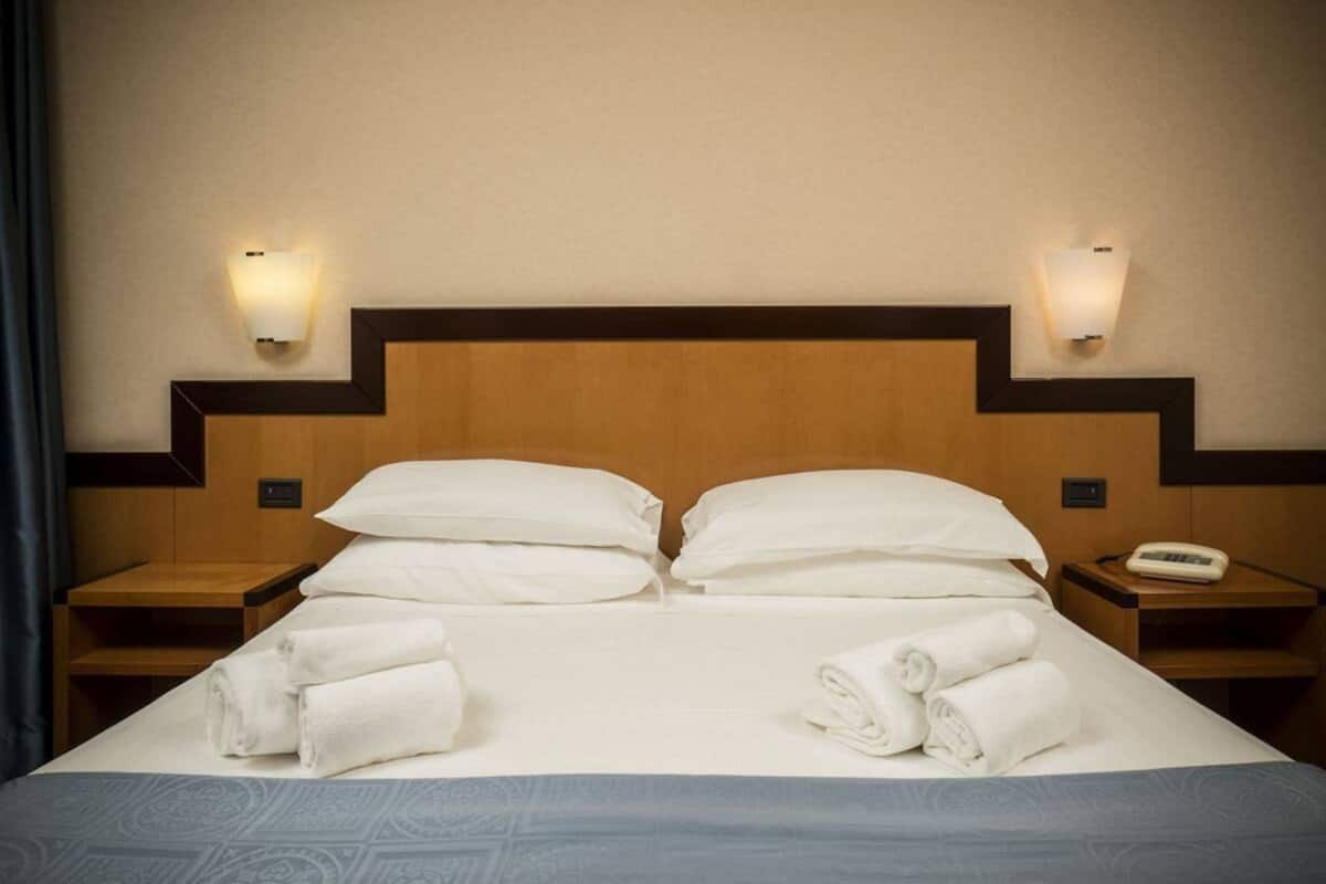 A hotel room with a bed, two bedside tables, a telephone, and two wall-mounted lamps.