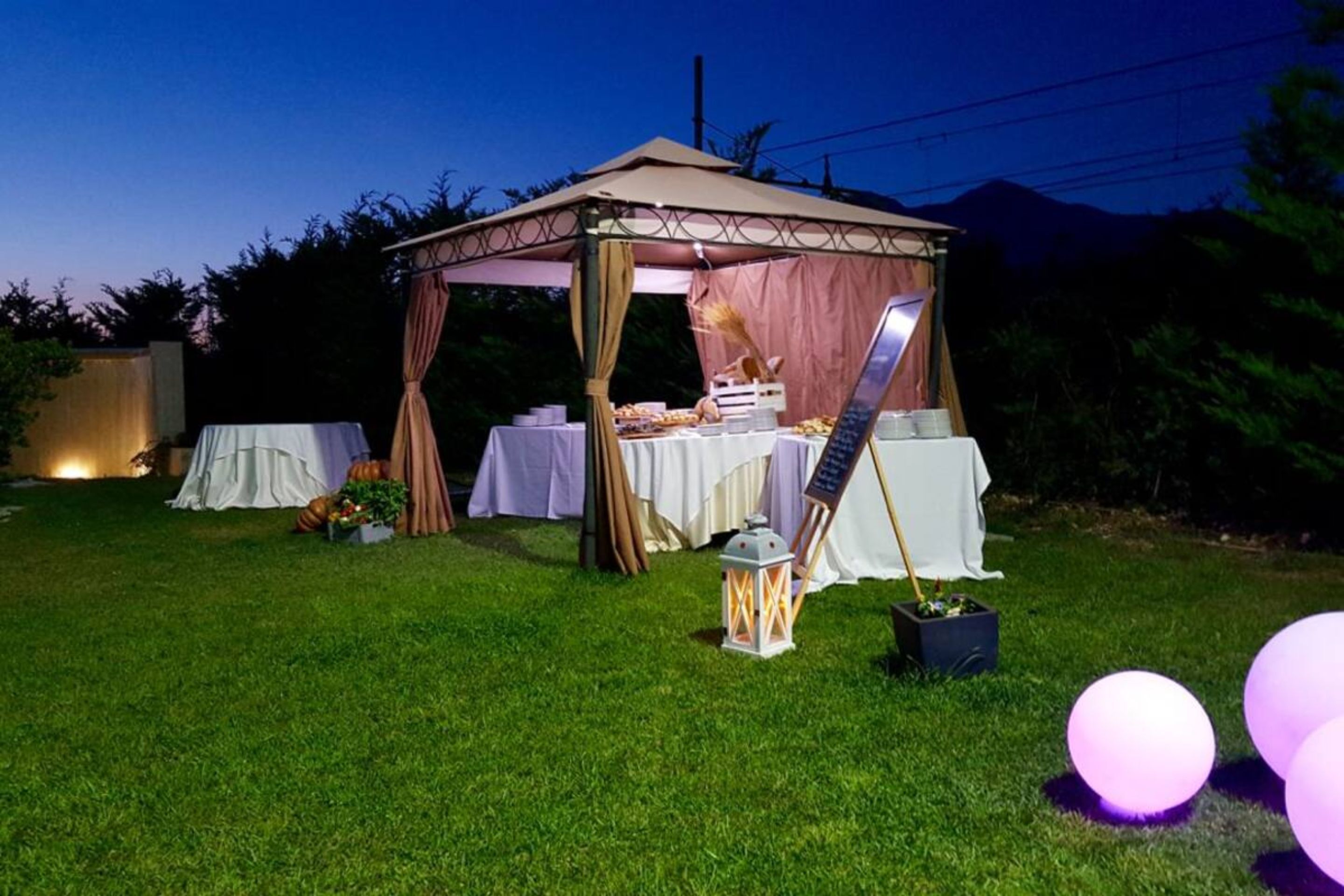 A gazebo with a table set up for an event, surrounded by grass and trees.