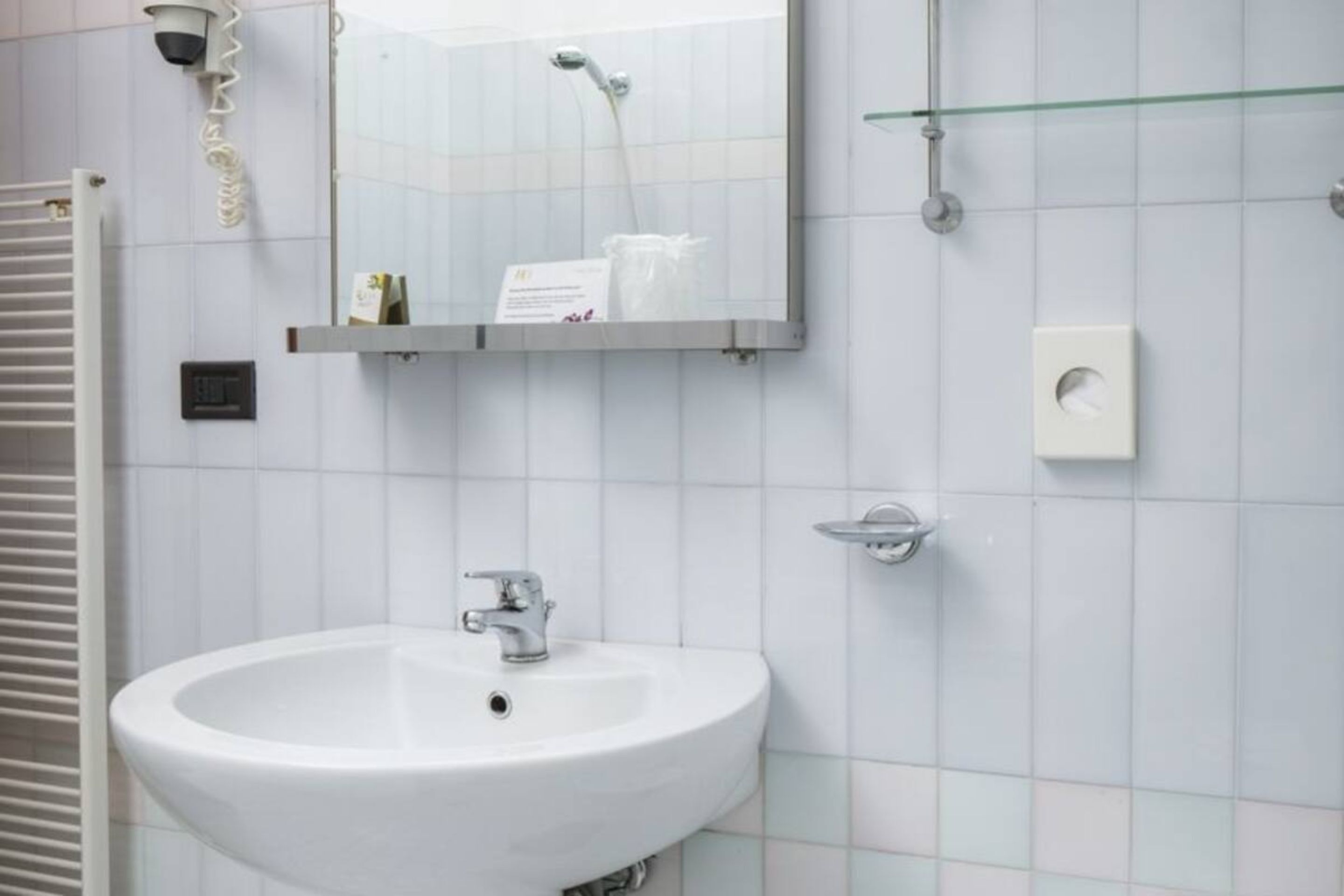 Ein Badezimmer mit Waschbecken, Spiegel, Dusche und einer Glasablage.