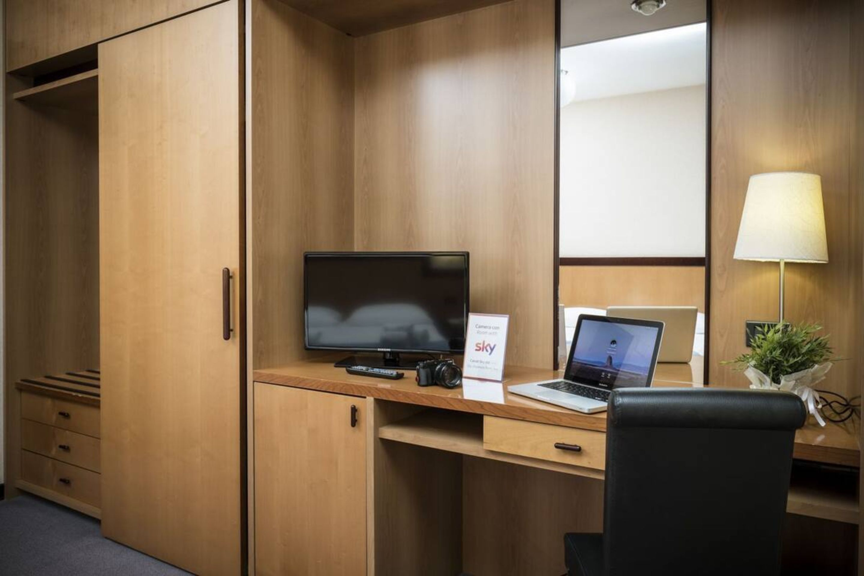 Una habitación de hotel con un escritorio de madera, una computadora portátil, un televisor y una cámara.