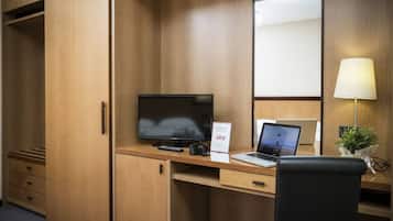 Una habitación de hotel con un escritorio de madera, una computadora portátil, un televisor y una cámara.