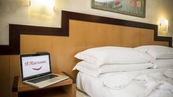 Una habitación de hotel con cabecera de madera, una computadora portátil sobre una mesita de noche y una cama con sábanas blancas.