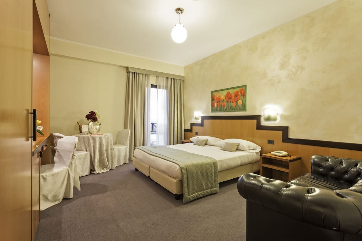 A hotel room with a bed, a sofa, a table with a vase of flowers, and a painting on the wall.