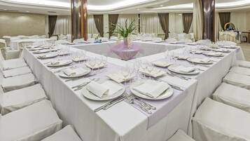A conference room with a long table set for a formal event, surrounded by white chairs.
