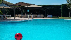 Piscina com uma bola vermelha flutuando, cercada por área de estar externa e um espaço coberto.