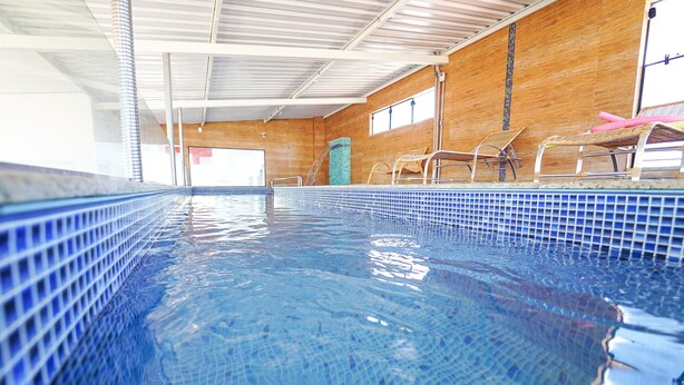 Una piscina interior con agua azul cristalina, paredes de madera y suelo de baldosas.