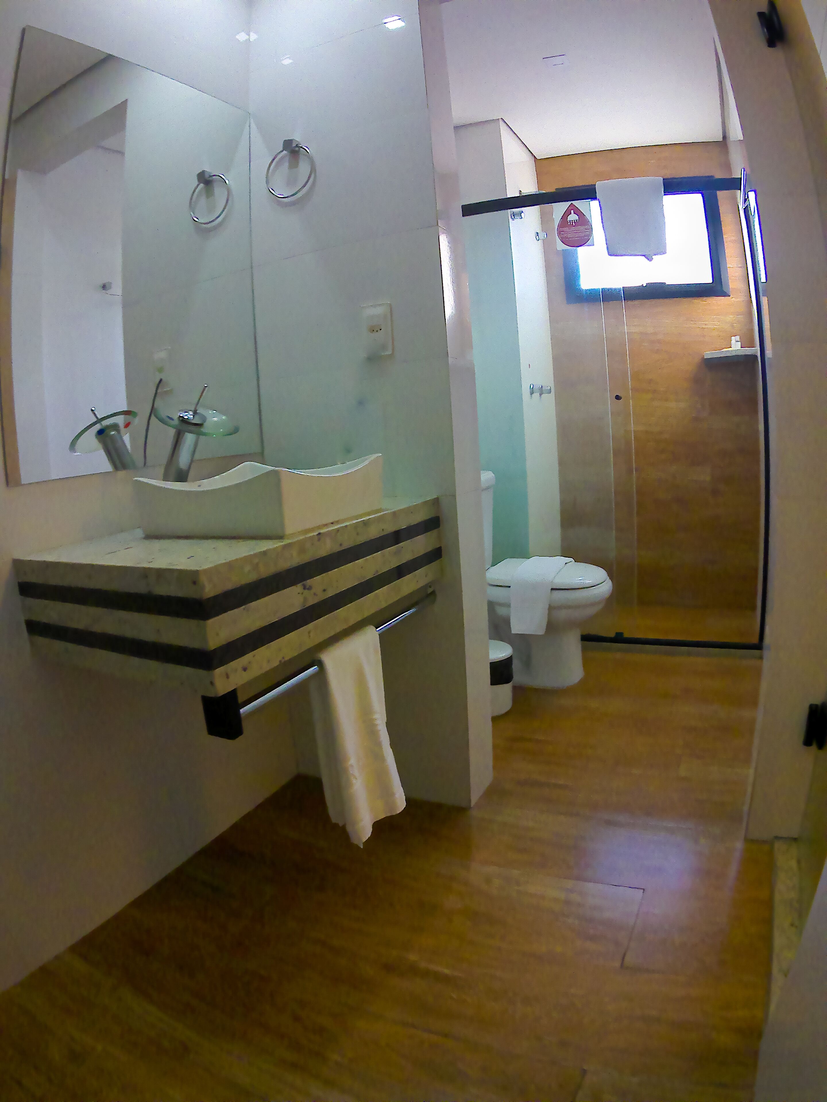 A modern bathroom with a large mirror, a glass sink, and a toilet.