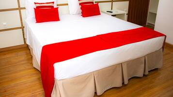 A neatly made bed with a red and white bedspread, a wooden floor, and a white wall with a wooden panel design.