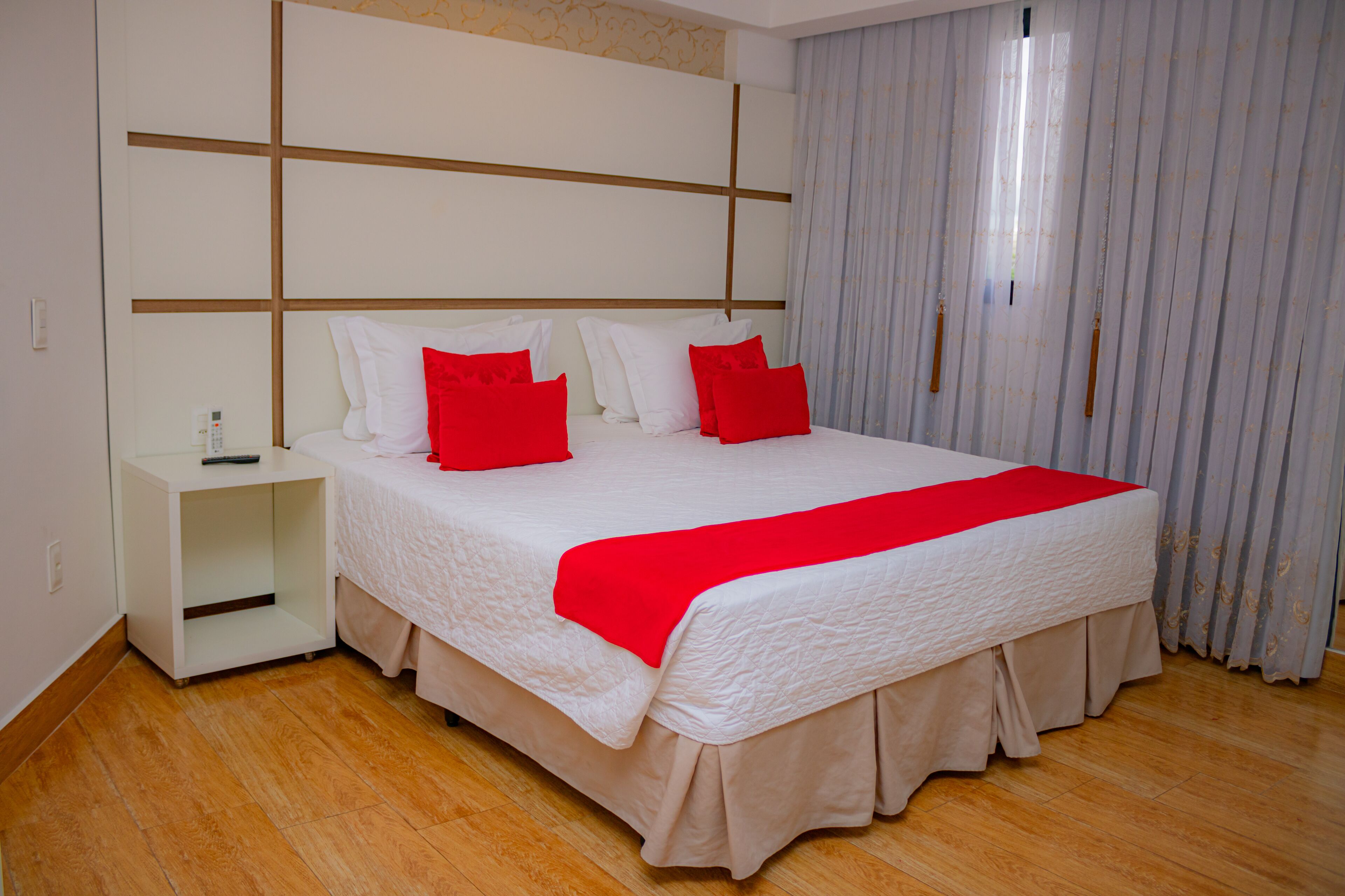 A neatly arranged hotel room with a large bed, a nightstand, and a window with curtains.