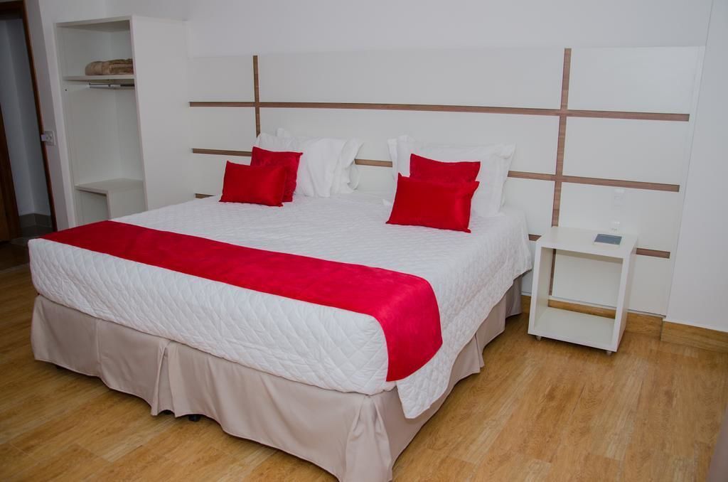 A neatly made bed with a white and red bedspread, two red pillows, and a wooden headboard.