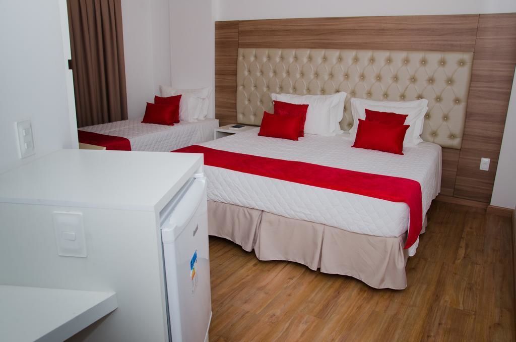 A hotel room with two beds, a wooden headboard, and a white refrigerator.
