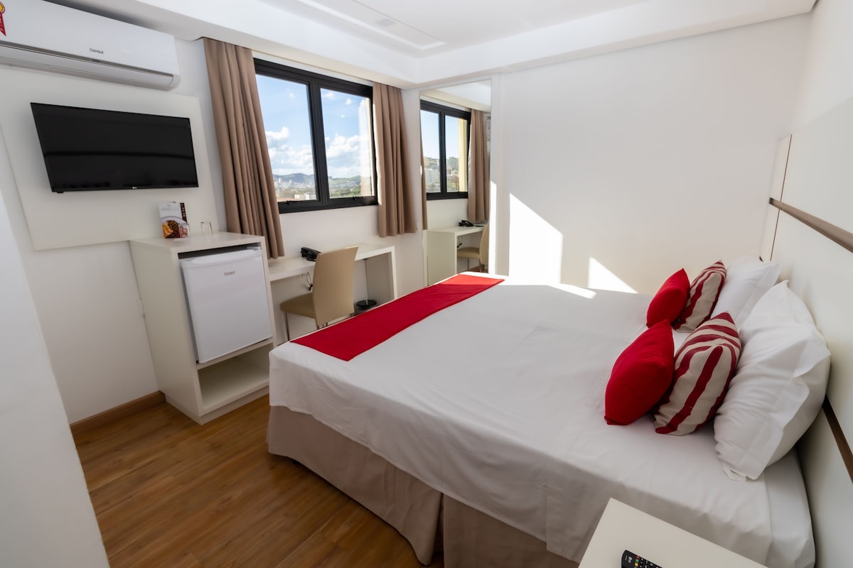 Una habitación de hotel con cama, escritorio, silla, televisor y minibar.