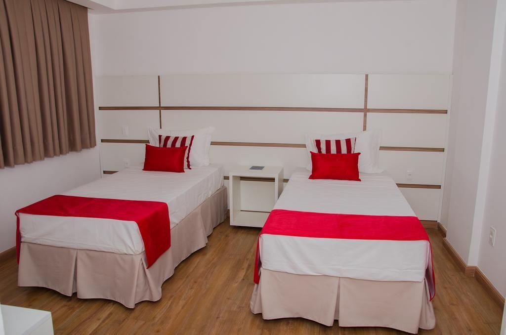 A hotel room with two beds, each with a red and white bedspread, a nightstand, and a wall-mounted headboard.