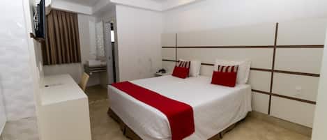 Una habitación de hotel moderna con una cama grande, una mesita de noche, un televisor y un baño visible a través de una puerta abierta.