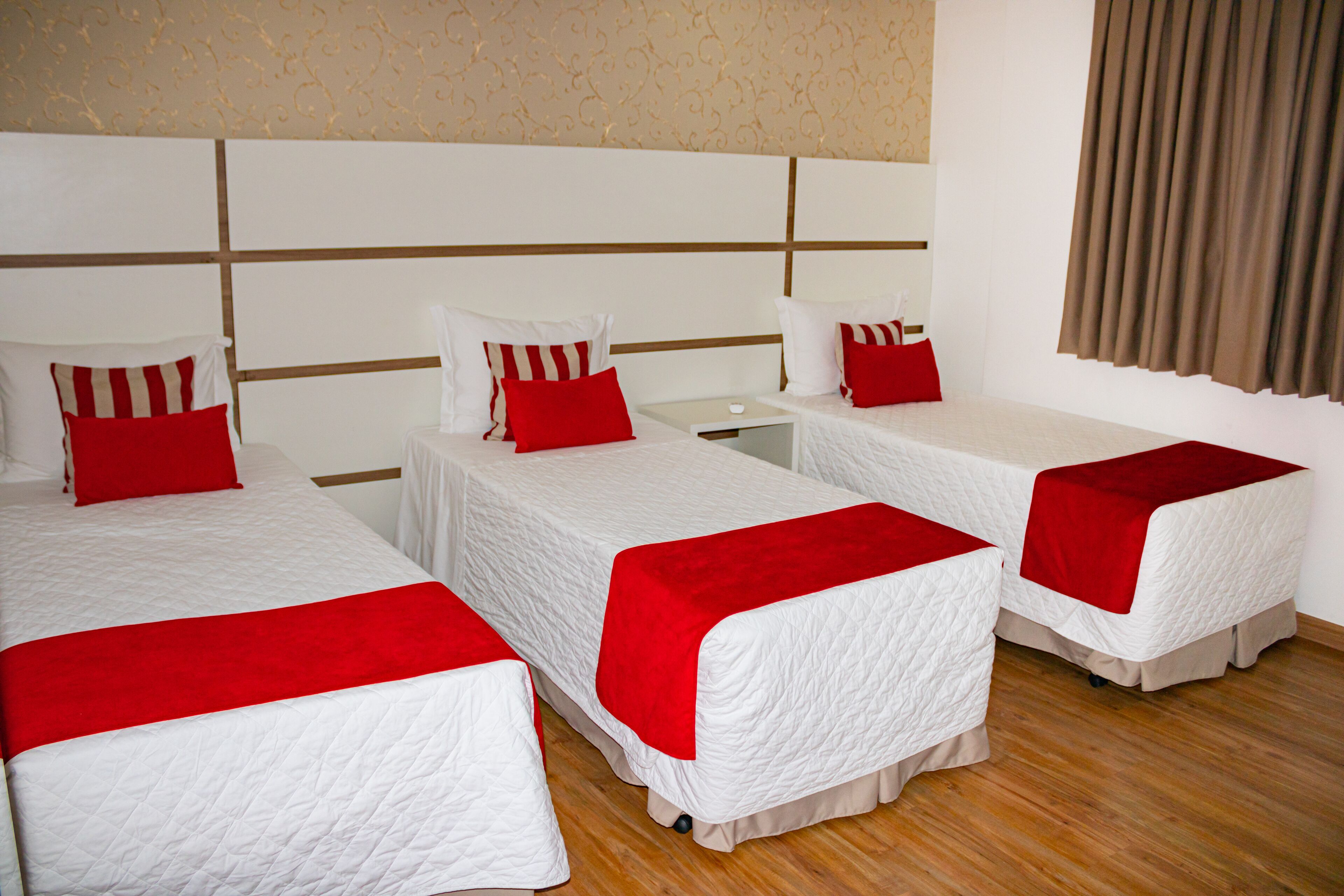 Een hotelkamer met drie bedden, elk voorzien van witte beddengoed en rode accenten.
