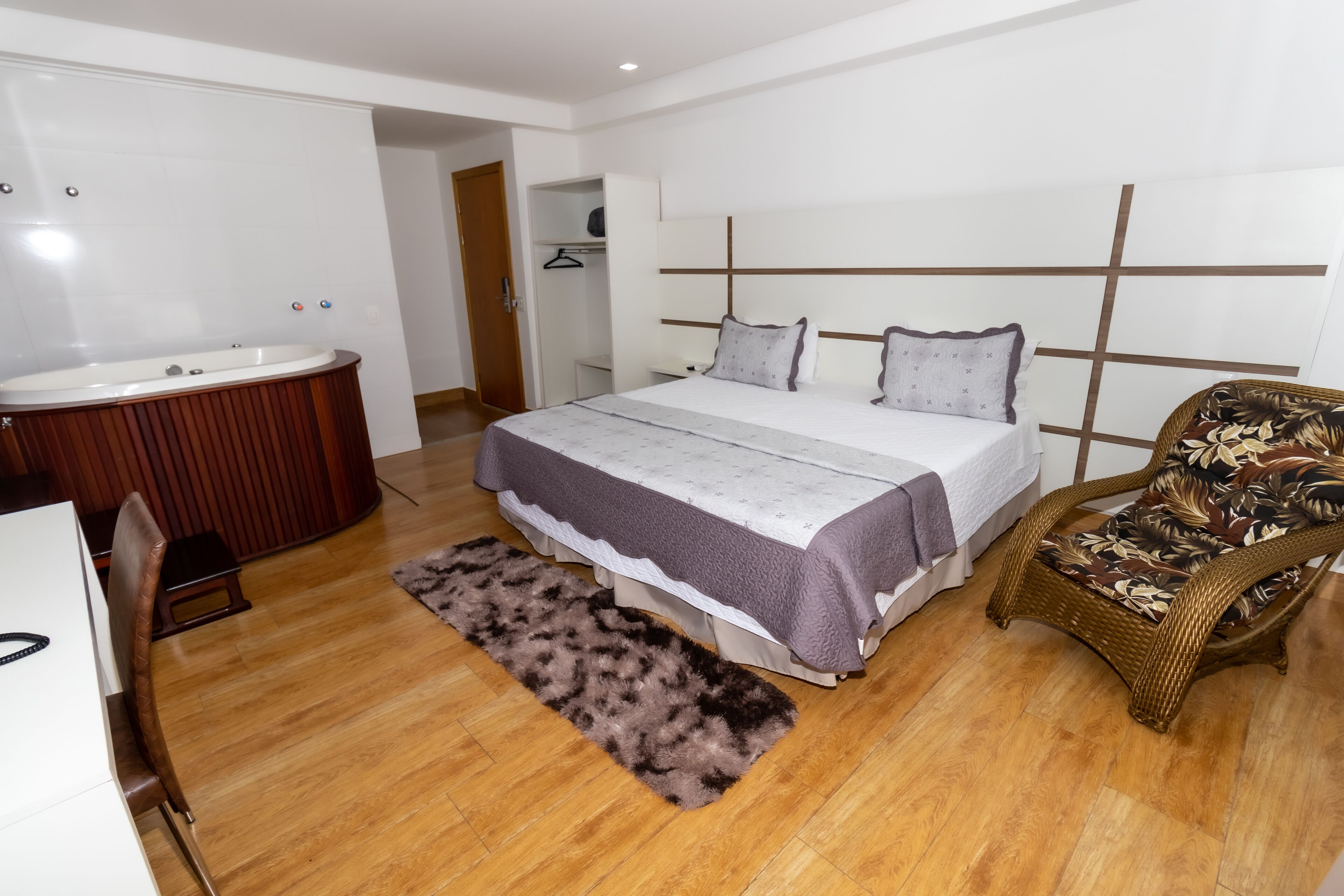 Une chambre avec un grand lit, une table de chevet, une chaise, une salle de bain avec une baignoire et un plancher en bois.