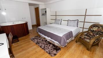 Une chambre avec un grand lit, une table de chevet, une chaise, une salle de bain avec une baignoire et un plancher en bois.