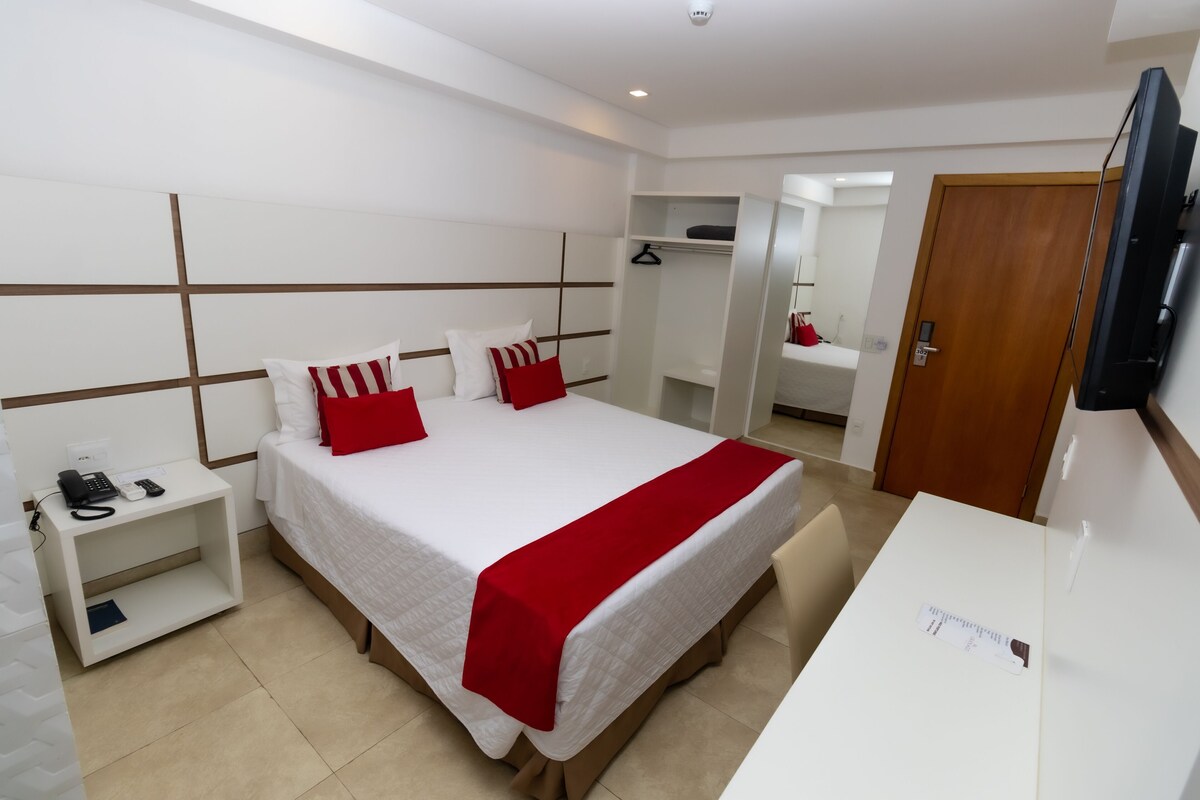 Una habitación de hotel con cama, mesita de noche, televisor y escritorio con silla.