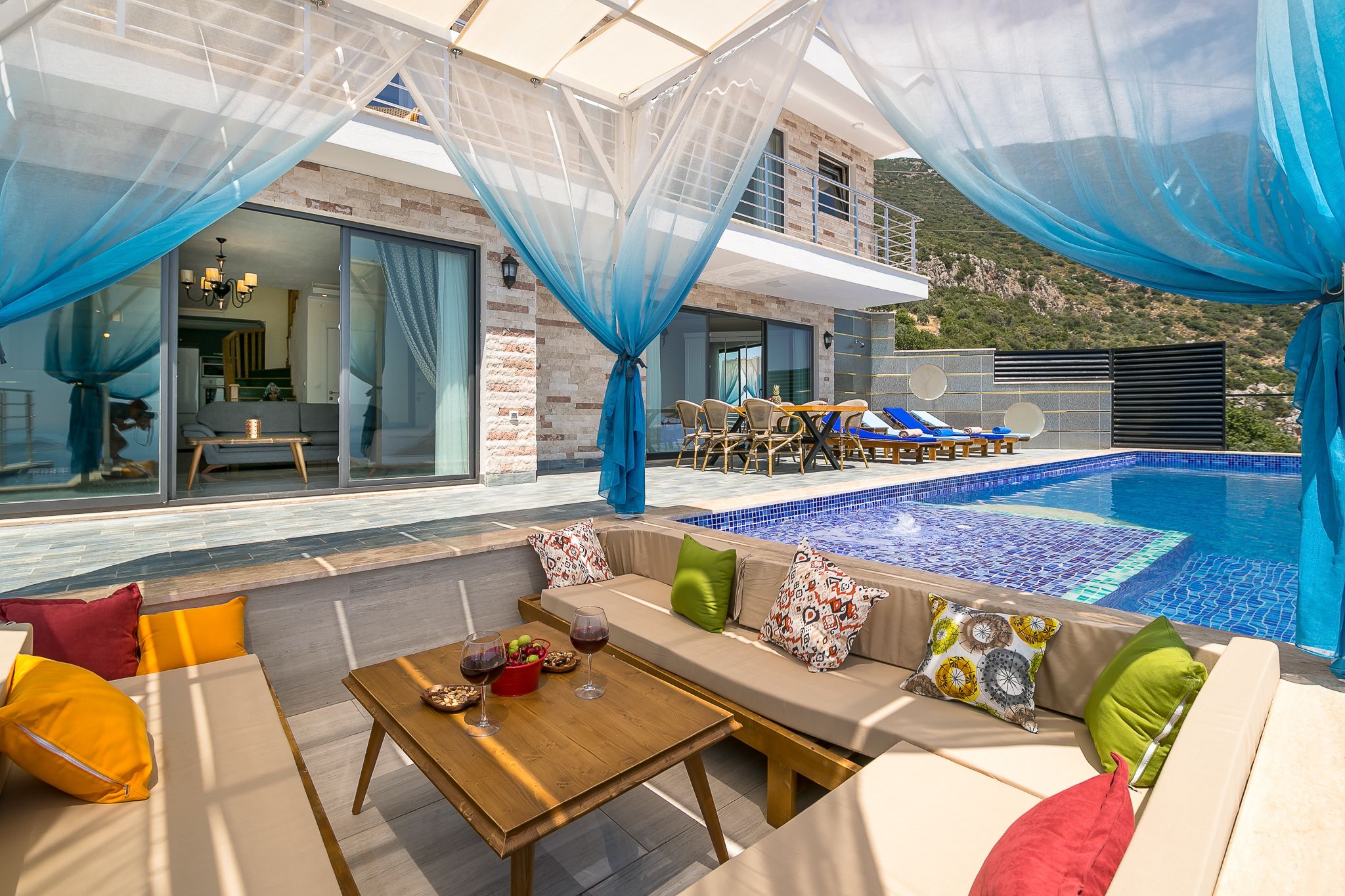 Ett modernt utomhusområde med pool, sittplatser och utsikt över bergen.