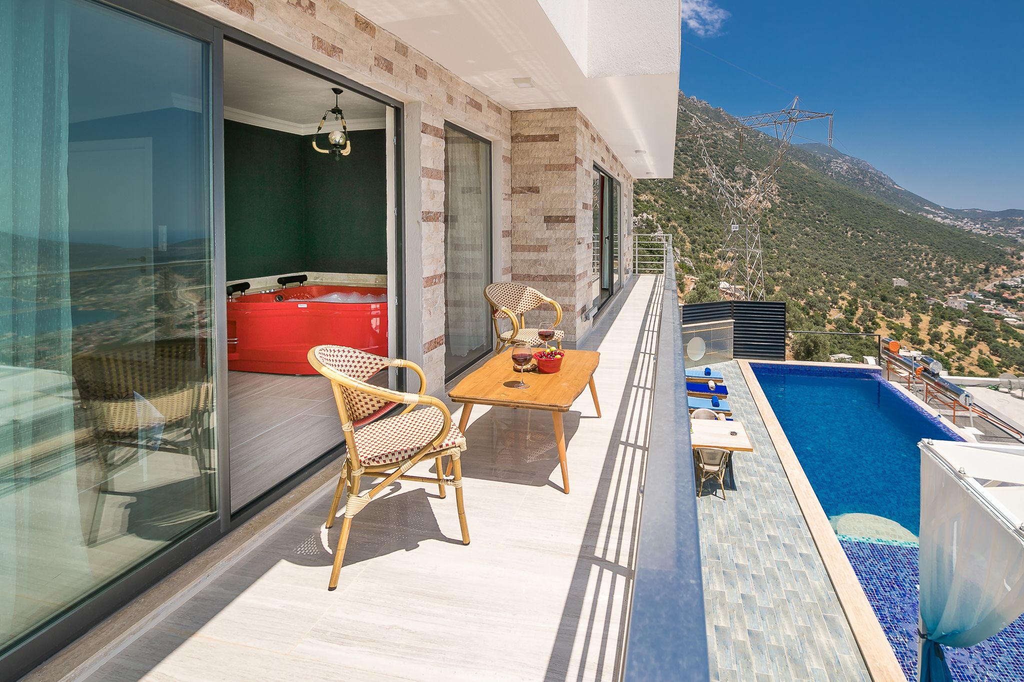 Un balcon avec une piscine, des fauteuils en osier, un canapé rouge et une table avec des bols.
