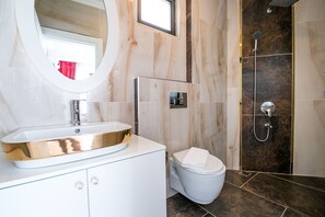 A modern bathroom with a large oval mirror, a white sink with a gold basin, a toilet, and a shower area. - Villa Paris Hill Villas Kalkan (Kas)