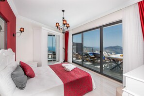 A modern hotel room with a large bed, a chandelier, a balcony with a table and chairs, and a view of the sea. - Villa Paris Hill Villas Kalkan (Kas)