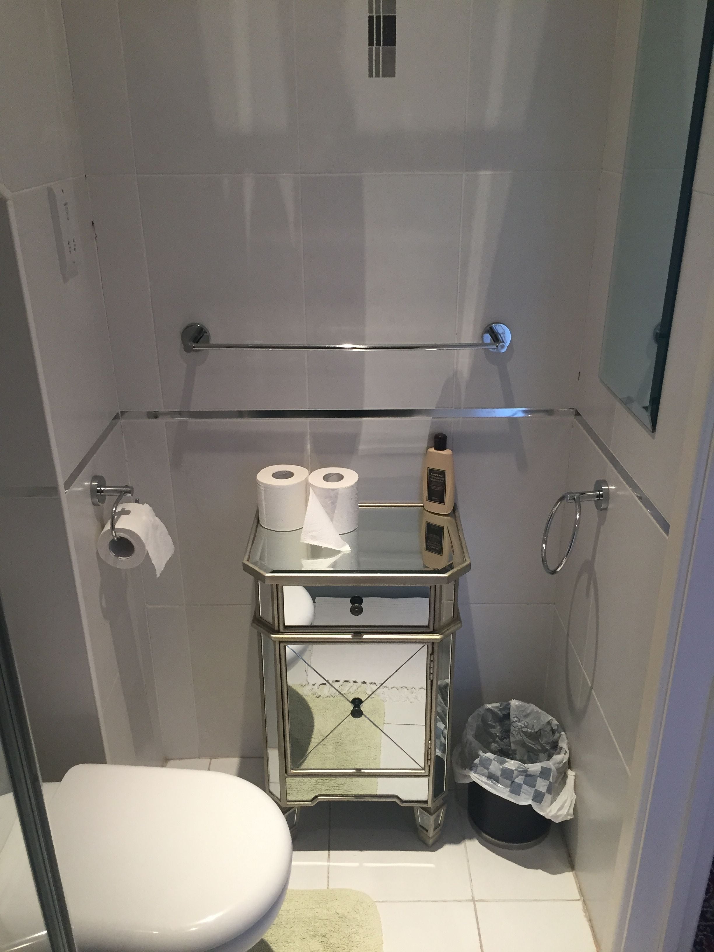 Un baño pequeño con azulejos, un inodoro, un tocador con tapa de vidrio y artículos de aseo, y un cubo de basura.