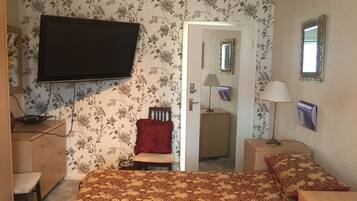 Une chambre à coucher comprenant un lit, un bureau, une chaise, une télévision, un miroir et une porte donnant sur une autre pièce.
