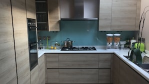 A modern kitchen with wooden cabinets, a gas stove, and a built-in oven. - Edgware Bed and Breakfast (Edgware)