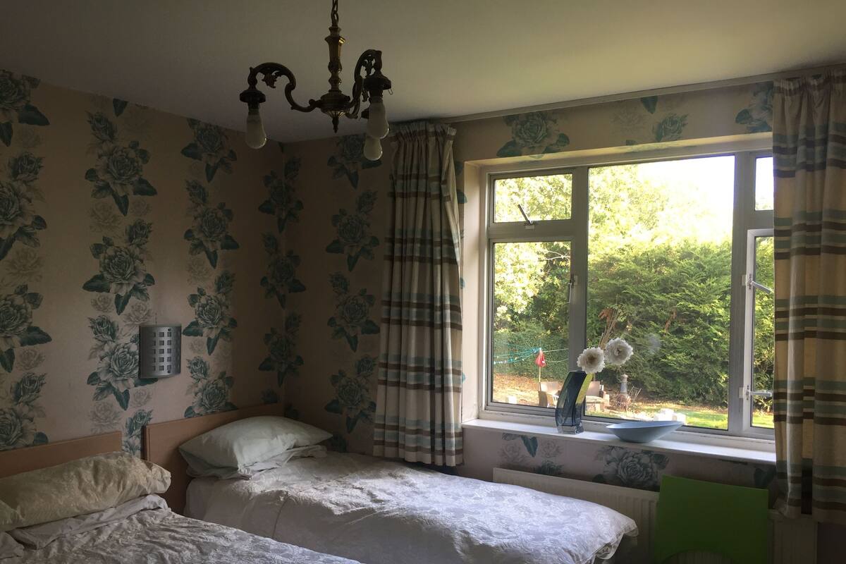 Un dormitorio con dos camas, una ventana con cortinas, un radiador y una silla verde.