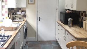 A compact kitchen with white cabinets, a washing machine, a stove, and a microwave. - Edgware Bed and Breakfast (Edgware)
