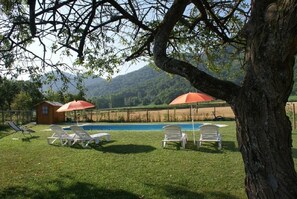 A poolside area with lounge chairs and umbrellas, surrounded by a wooden fence and a mountain backdrop. - Mas Prat (La Vall de Bianya)
