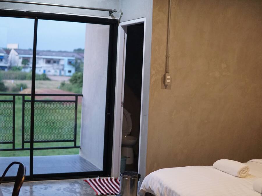 Ein Schlafzimmer mit Bett, Fenster und Blick auf ein Gebäude und Grünflächen.