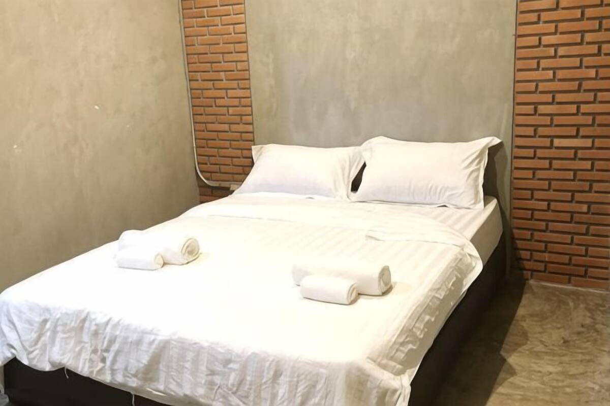 Un lit simple avec du linge de lit blanc et un mur en briques.