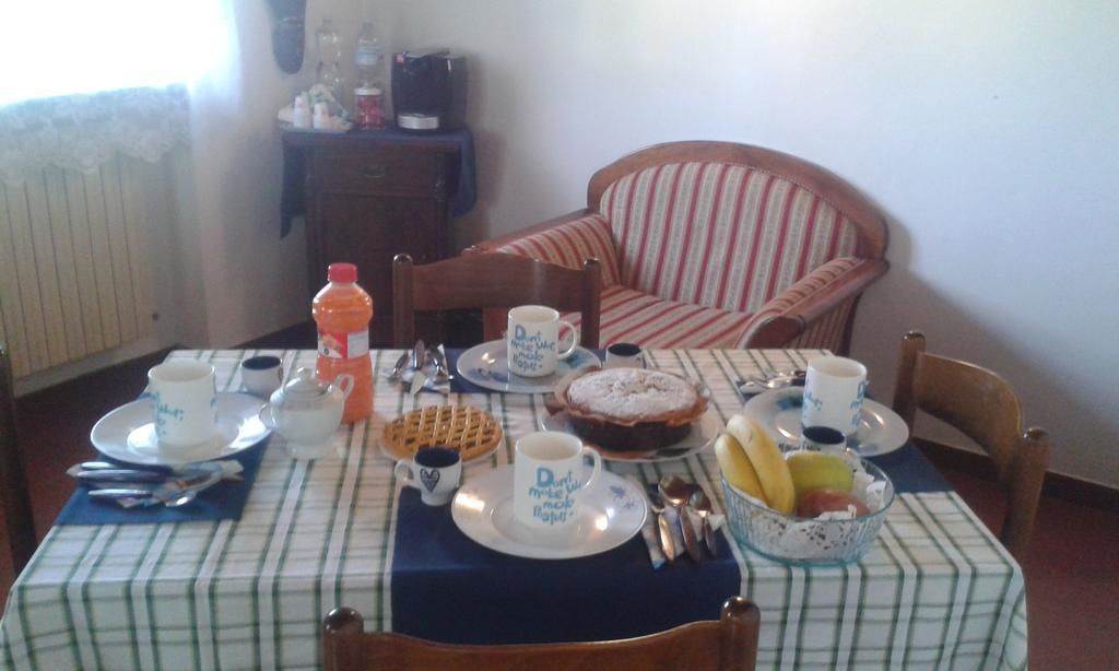Une table à manger dressée avec des assiettes, des tasses, des couverts, un gaufre, un gâteau et un saladier de fruits.