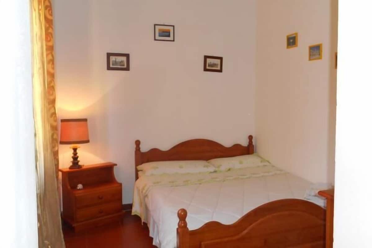 A bedroom with a wooden bed, a nightstand with a lamp, and three framed pictures on the wall.